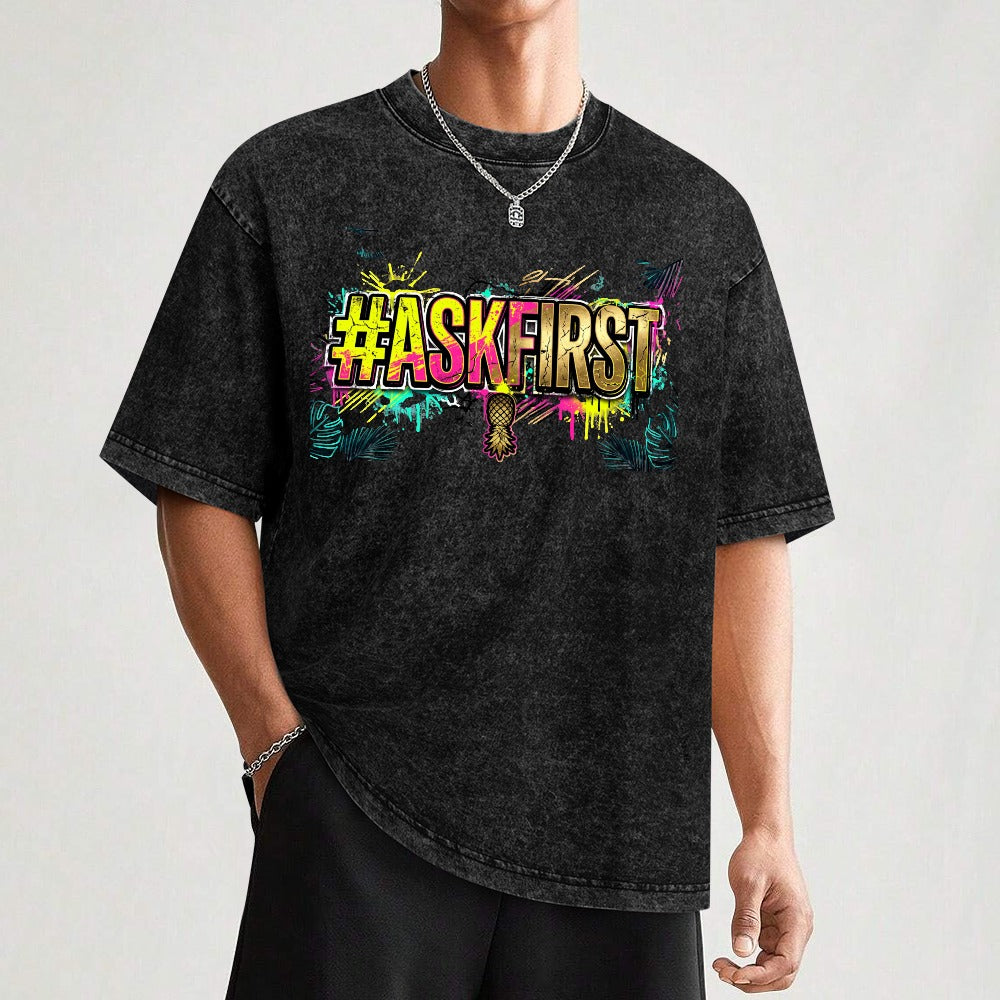 Man standing with a weathered black & gray shirt with #ASKFIRST in bright colors on the front with a silver chain around his neck.
