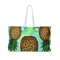 A tote bag featuring a bold graphic print of three pineapples with leopard-print bodies and green leafy tops on a light turquoise background, with white rope handles.