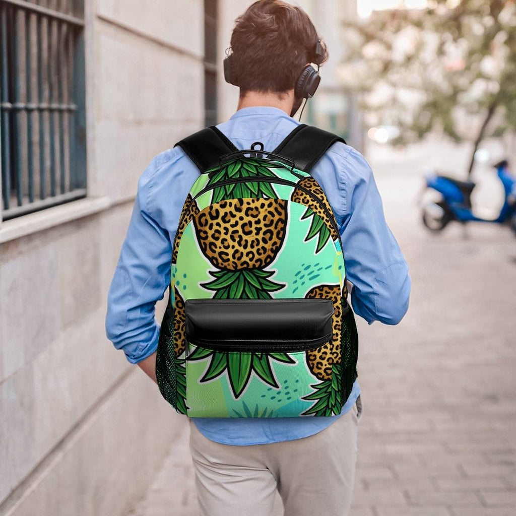 A person viewed from behind walking on a sidewalk, wearing a backpack with a tropical pineapple print in green and yellow on a mint background, along with a light blue shirt and beige pants.