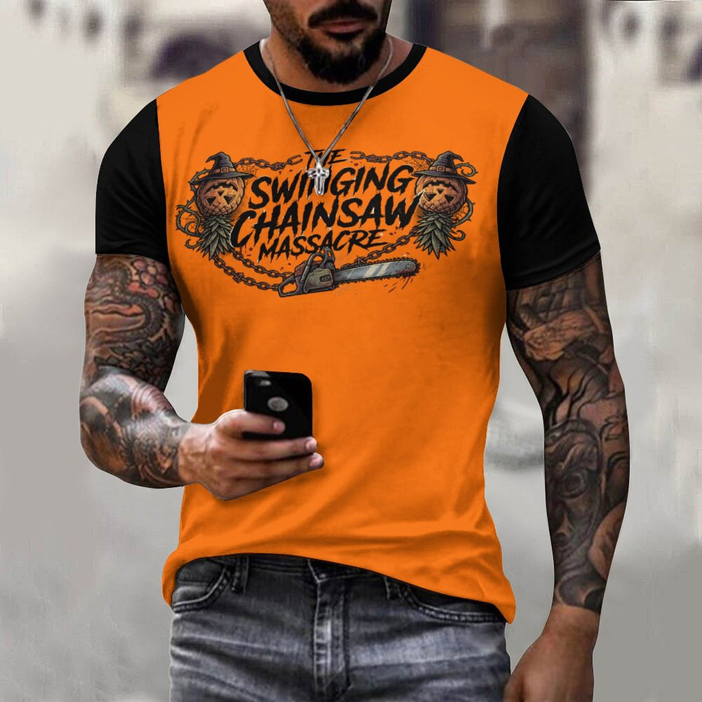 A man wearing a bright orange and black raglan t-shirt with a graphic print that reads 'The Swinging Chainsaw Massacre' featuring cartoon chainsaw and bear illustrations. He is holding a black smartphone and wearing gray jeans, set against a blurred gray background.