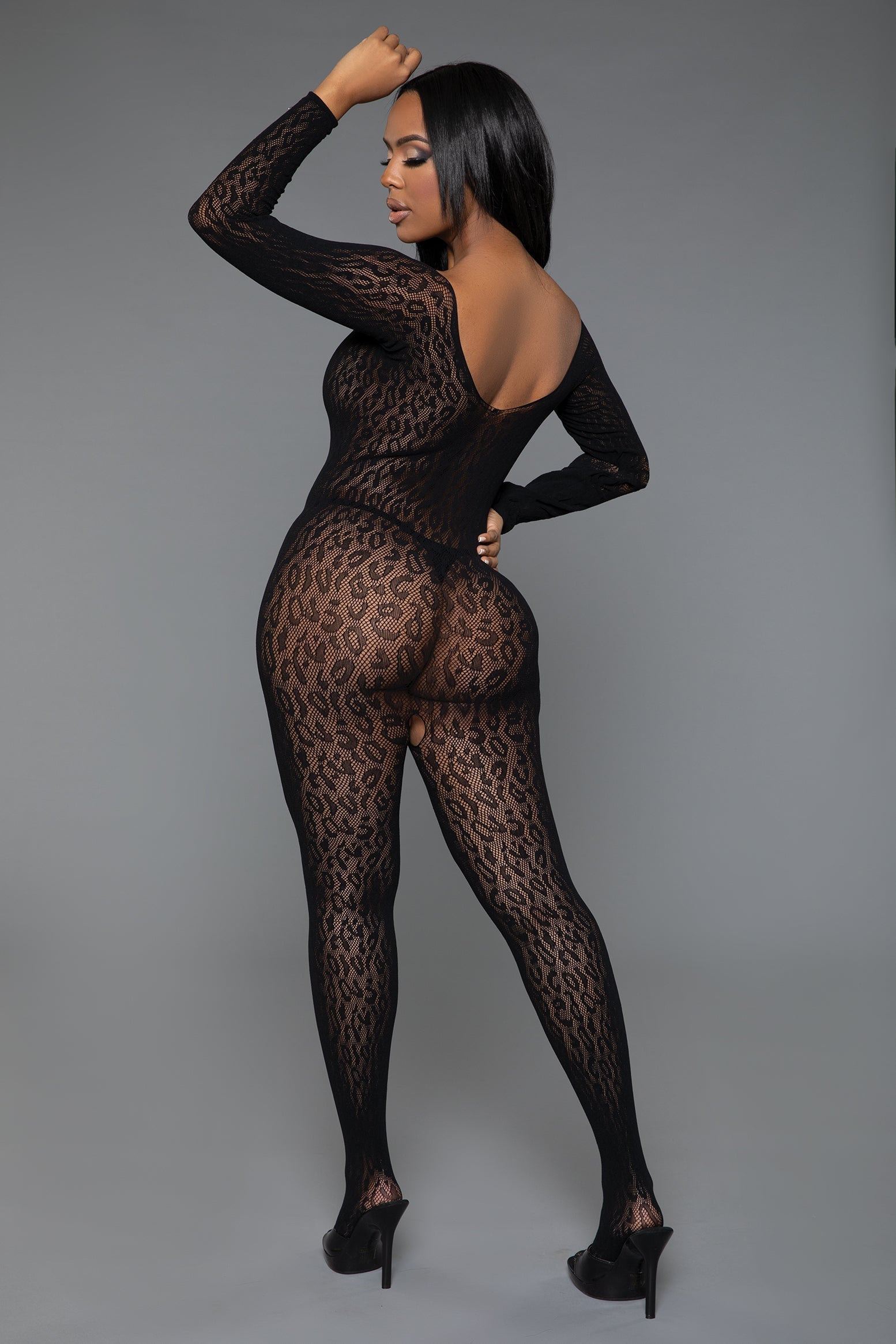 Model wearing a black lace bodystocking against a gray background