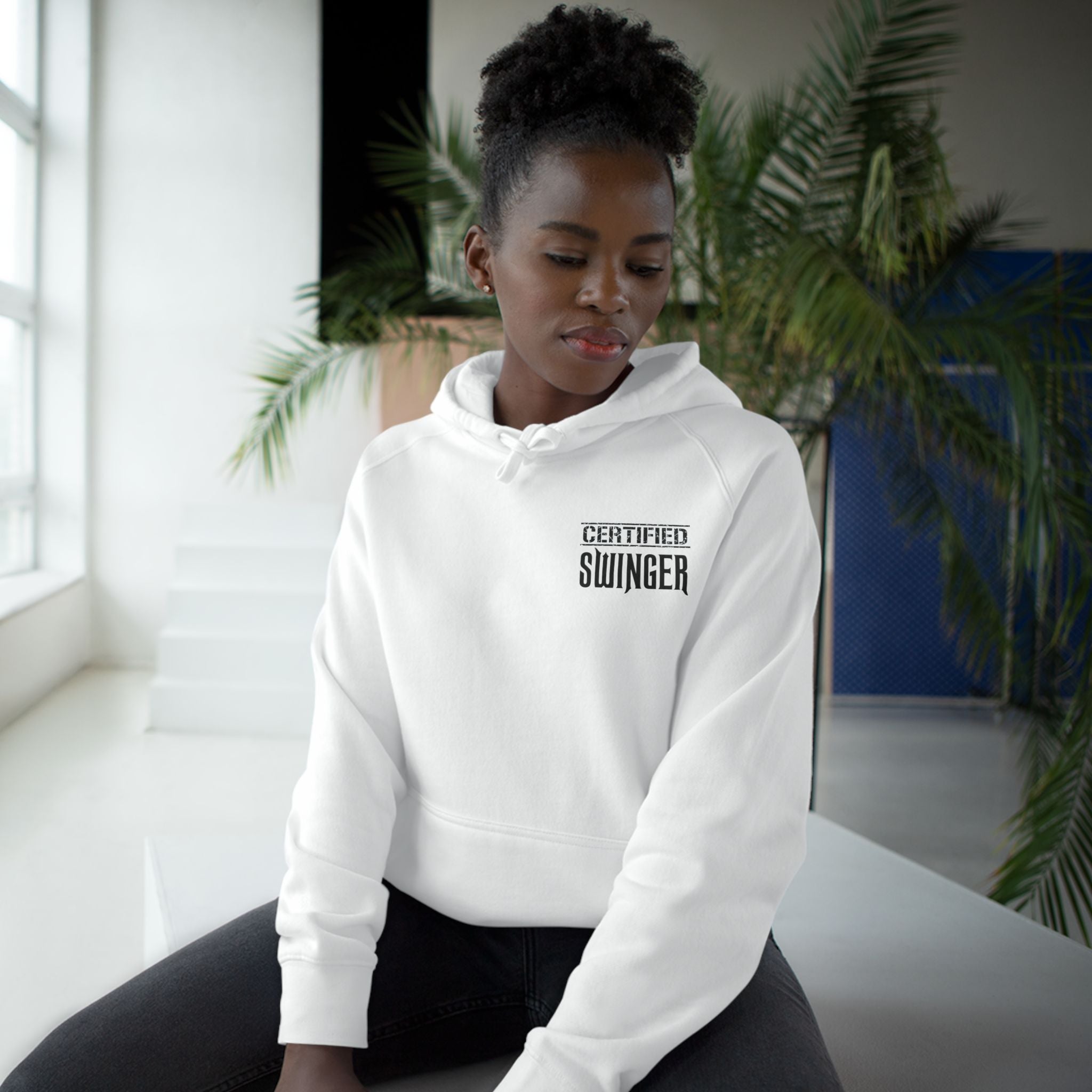 A woman sitting and wearing a white hoodie with 'CERTIFIED SWINGER' text on the front.