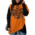 A woman wearing a long-sleeve hoodie with a bright orange body, black sleeves and hood, featuring a large graphic print on the front that reads 'The Swinging Chainsaw Massacre' with a chainsaw, skulls, and decorative illustration.
