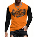 A man wearing a long-sleeve t-shirt with a bright orange body and black sleeves, featuring a graphic print of two cartoon skulls with chainsaws and the text 'THE SWINGING CHAINSAW MASSACRE'.