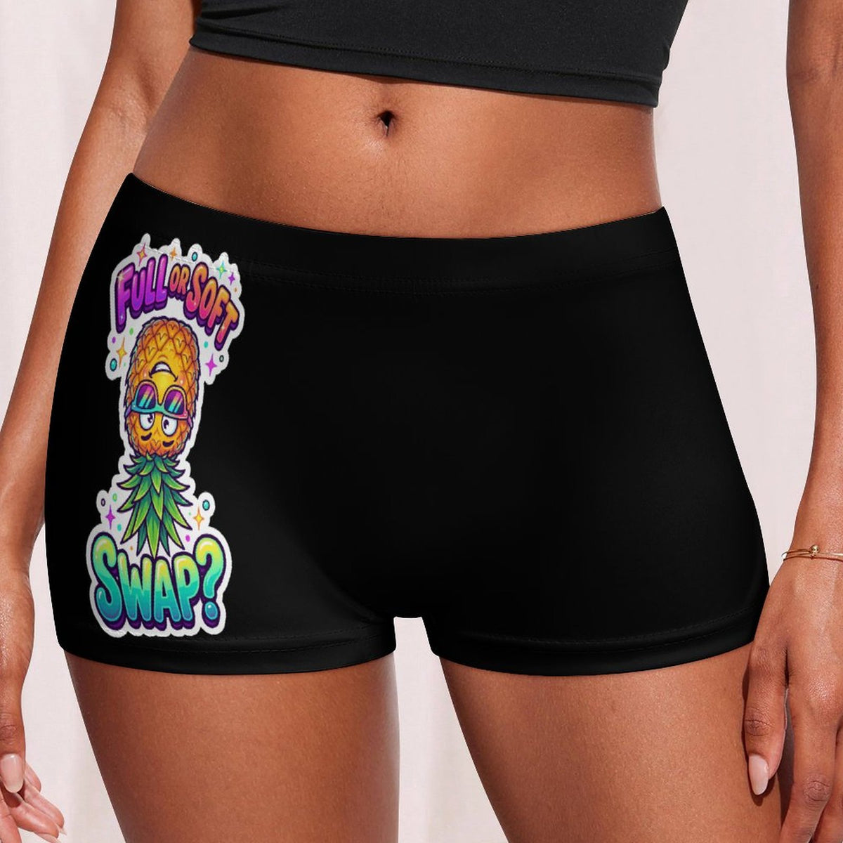 Black athletic boyshorts worn by a model, featuring a colorful graphic of a pineapple character wearing sunglasses with the text 'FULL SOFT SWAP?' in vibrant pink, yellow, green, and blue lettering.