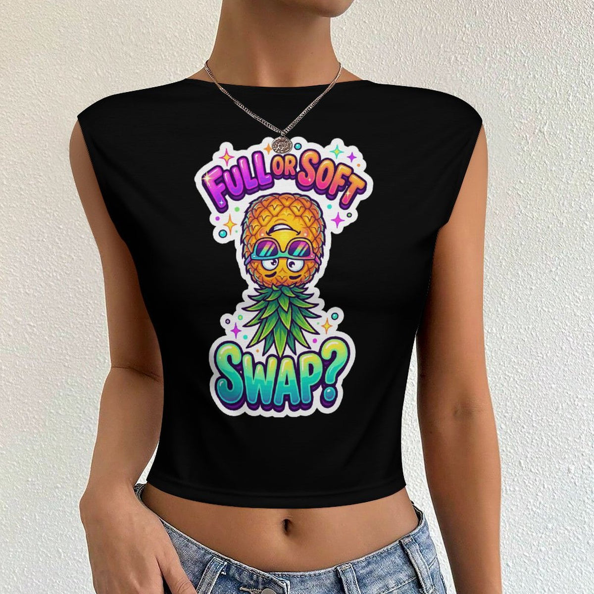 A woman wearing a black crop top with a colorful pineapple graphic and the text 'FULL OR SOFT SWAP?' on the front, paired with light blue denim jeans against a textured off-white wall.
