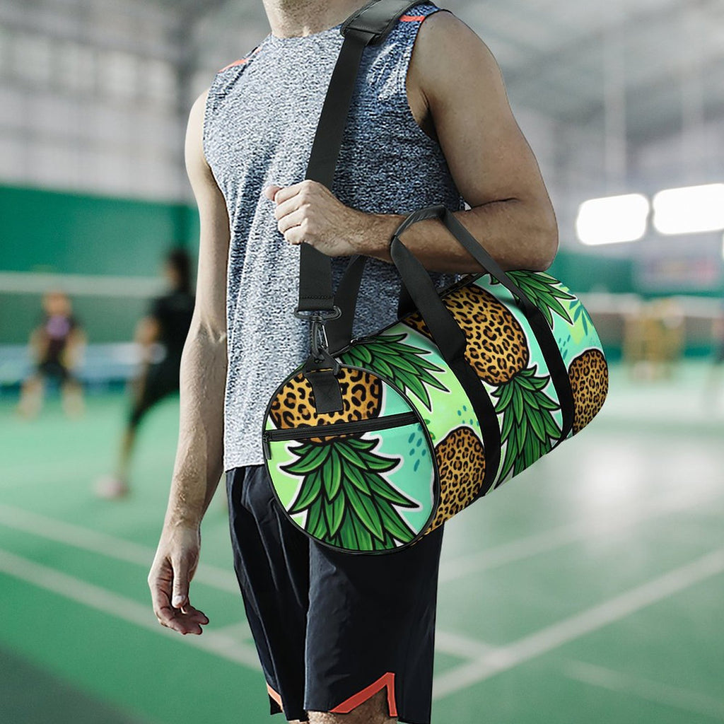 A man at a badminton court carries a colorful duffel bag over his shoulder. The bag features a tropical design with pineapples, leopard print details, and a mint green background.