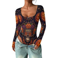 A woman wearing a long-sleeve scoop-neck bodysuit with a colorful Day of the Dead sugar skull and jack-o'-lantern print on a black background, paired with light-wash denim jeans.