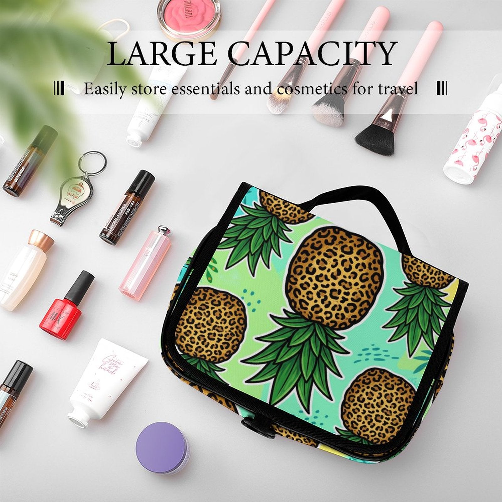 A large capacity travel makeup bag with a colorful pineapple and leopard print pattern, displayed in a styled flat-lay arrangement with cosmetics and brushes on a light gray background.