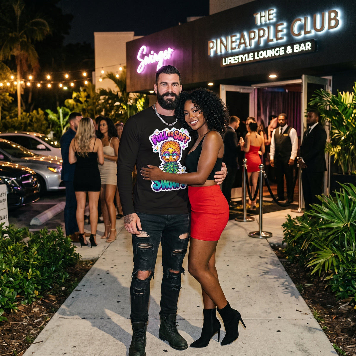 A man and a woman posing together in front of The Pineapple Club lifestyle lounge and bar at night. The man wears a black graphic t-shirt, ripped black jeans, and black boots, while the woman wears a black top, a bright red mini skirt, and black ankle boots.
