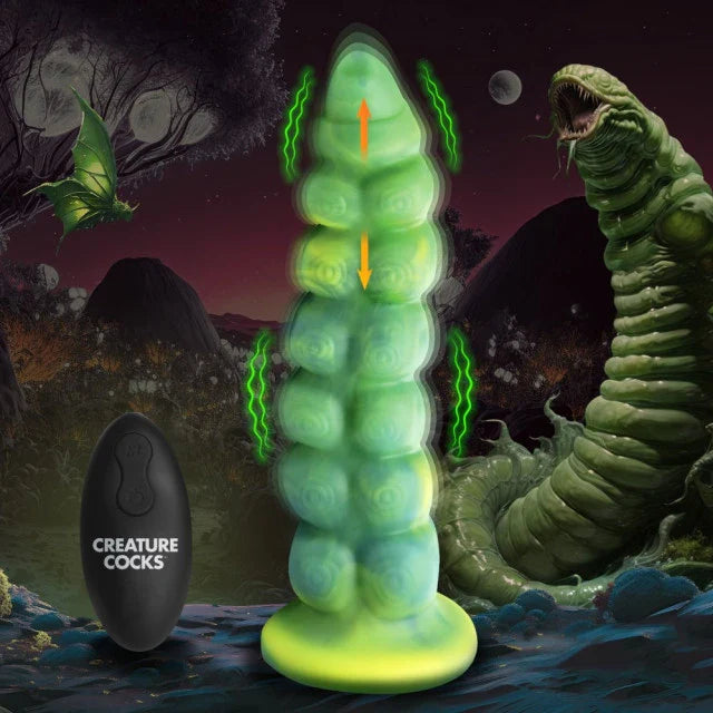 Toy resembling a large green caterpillar with a smaller black toy labeled 'Creature Cocks' against a fantasy landscape background.