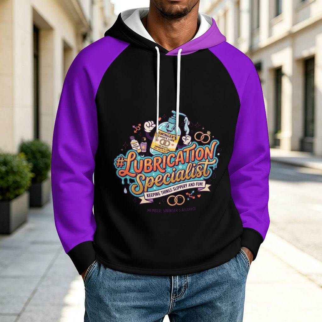 A man wearing a black and purple raglan hoodie with a colorful 'Lubrication Specialist' graphic on the front, standing on a city sidewalk.