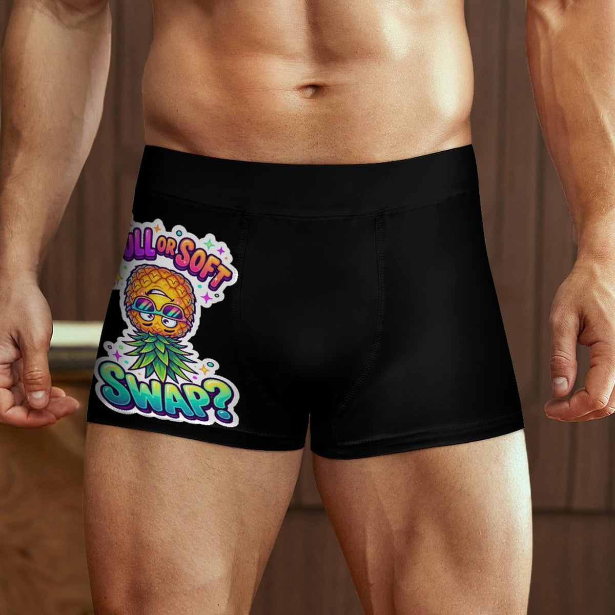 A close-up of a man's lower torso wearing black boxer briefs with a colorful graphic on the front. The graphic features a pineapple character wearing sunglasses and a green leaf crown, with the text 'ALL IS SOFT' above and 'SWAP?' below in a stylized multicolor font.