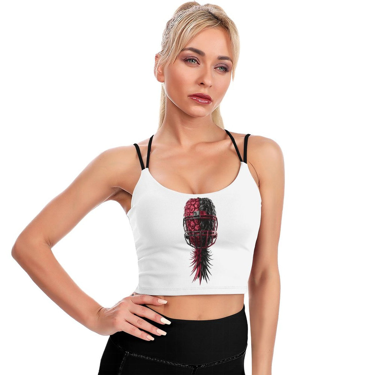 A blonde woman modeling a white crop top tank with black spaghetti straps and a central graphic of a black and red patterned soccer ball with a red feather, paired with black athletic bottoms, against a plain white background.