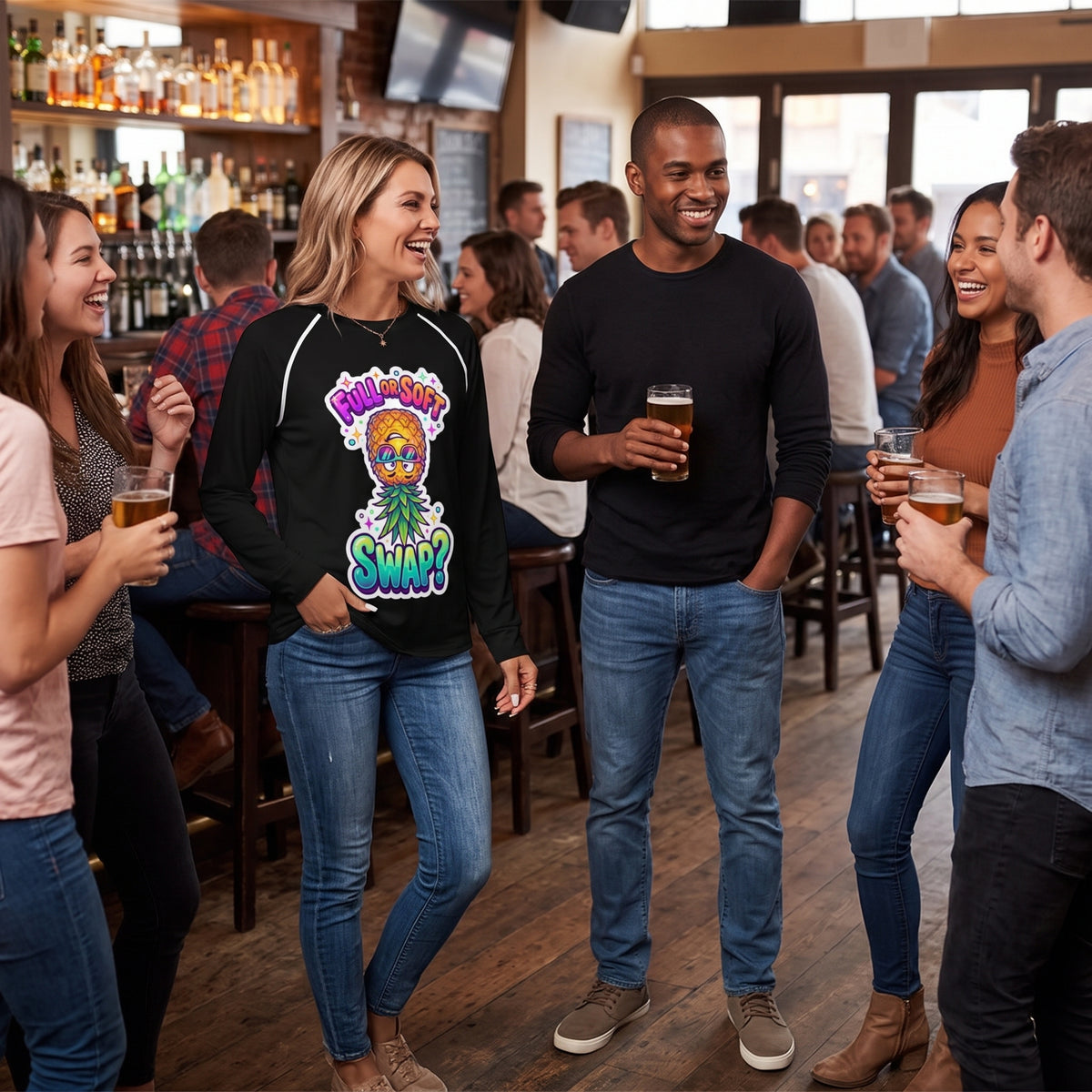 Woman wearing a black ‘Full or Soft Swap?’ pineapple graphic shirt and jeans, laughing with friends over beers at a lively bar.